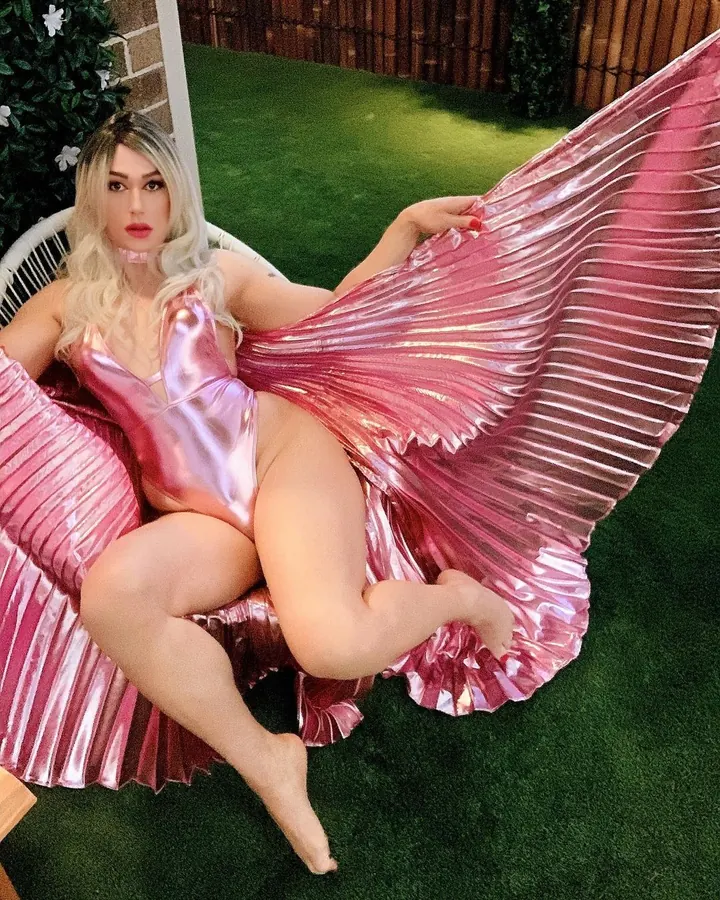 Femme trans aux cheveux blonds, portant un haut noir, regardant l'objectif dans un cadre intérieur.
