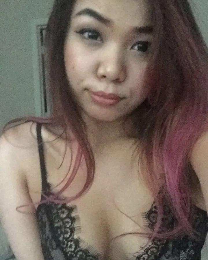 Femme trans en lingerie noire, regardant l'appareil, cheveux roses et bruns.