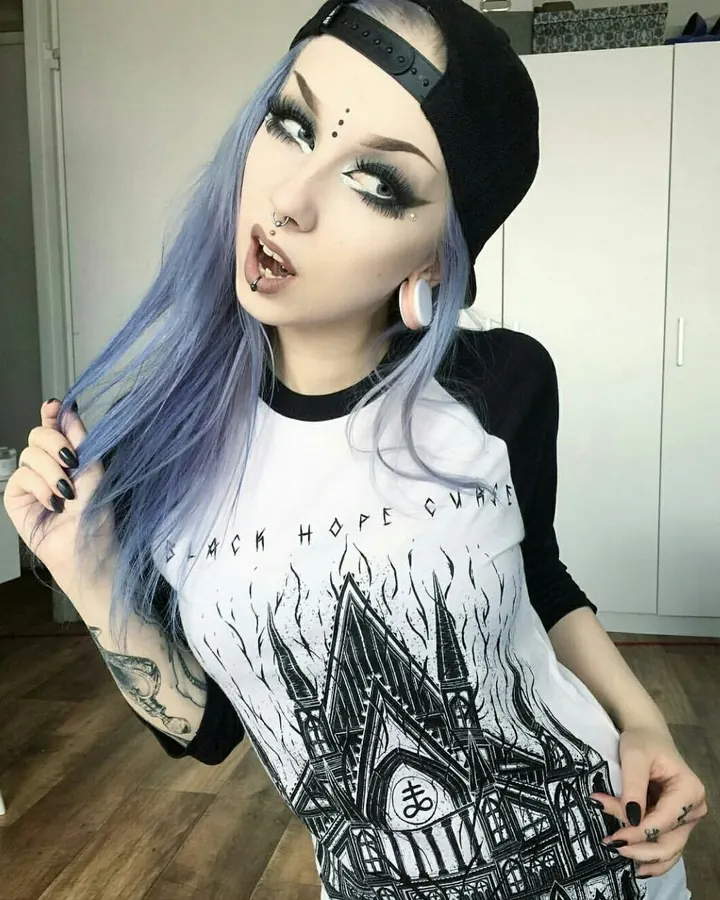 Femme trans européenne aux cheveux gris, portant un haut noir, assise sur un canapé rouge, regardant l'appareil photo.
