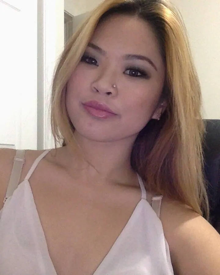Femme trans en haut blanc, assise sur une chaise, regard direct, cheveux longs, ambiance intime
