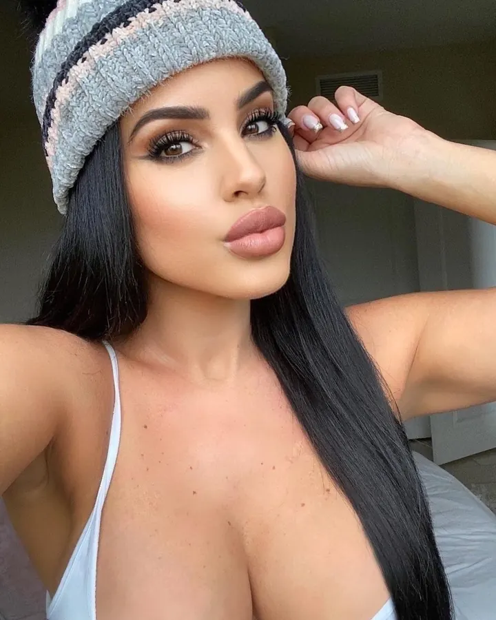 Femme trans en haut blanc, assise sur une chaise, regard direct, cheveux longs, ambiance intime
