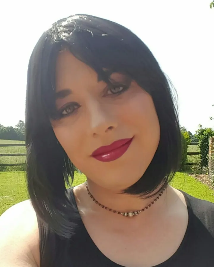 Femme trans aux cheveux bruns, portant un haut noir, les mains sur les hanches.