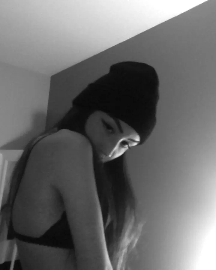 Femme trans aux cheveux bruns, prenant un selfie, portant un haut rose et un jean.