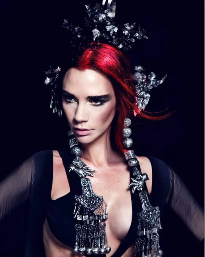 Femme trans aux cheveux roux, portant un haut noir, posant avec un regard intense et un sourire espiègle.